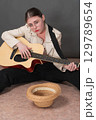 Sad woman guitarist street musician playing acoustic guitar and looking hopefully at camera. Young woman sits with legs apart and empty straw hat lies in front of her for donation for playing guitar 129789654