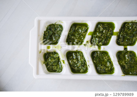 White ice cube tray filled with vibrant green pesto. Homemade fresh pesto sauce, prepared in portions, ready to freeze and store 129789989