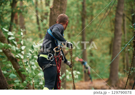 Process of preparing. Man is doing climbing in the forest by use of safety equipment 129790078