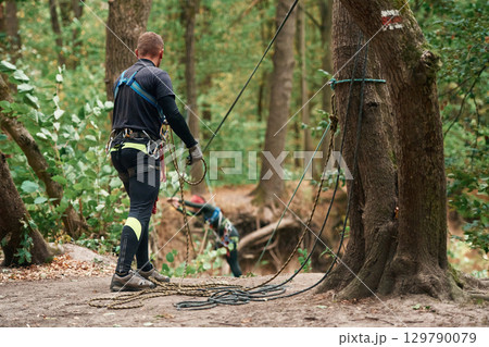 Process of preparing. Man is doing climbing in the forest by use of safety equipment 129790079