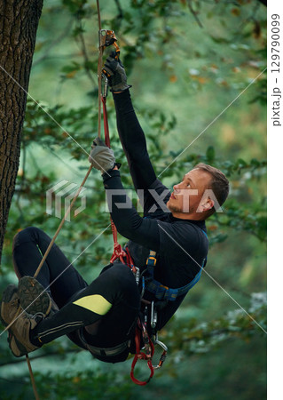 Side view, using the rope, hanging. Man is doing climbing in the forest by use of safety equipment 129790099