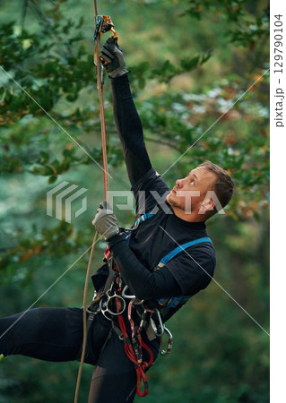 Man is doing climbing in the forest by use of safety equipment Man is doing climbing in the forest by use of safety equipment 129790104