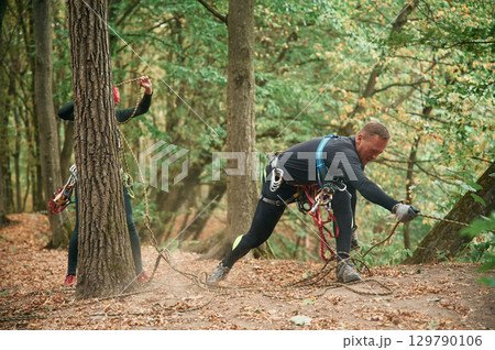 Standing on the ground and preparing. Man is doing climbing in the forest by use of safety equipment 129790106