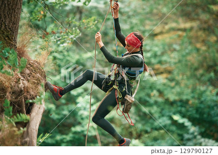 View from the side, hanging on the rope. Woman is doing climbing in the forest by the use of safety equipment 129790127