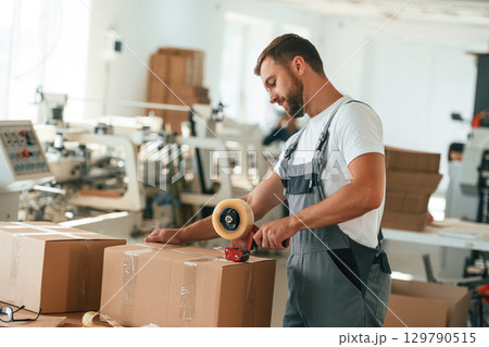 Using tape, packing the product. Handsome man is working at the factory of creating eco boxes 129790515