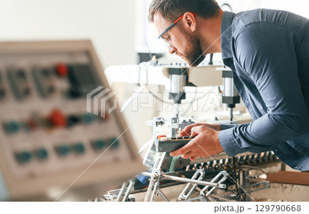 Operating the machine. Handsome man is working at the factory of creating eco boxes Operating the machine. Handsome man is working at the factory of creating eco boxes 129790668