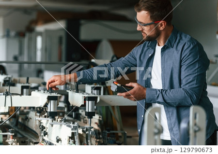 Working with machine. Handsome man is at the factory of creating eco boxes Working with machine. Handsome man is at the factory of creating eco boxes 129790673