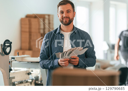Holding cardboards. Handsome man is working at the factory of creating eco boxes 129790685
