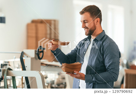 Cardboards in hands. Handsome man is working at the factory of creating eco boxes Cardboards in hands. Handsome man is working at the factory of creating eco boxes 129790692
