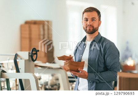 Cardboards in hands. Handsome man is working at the factory of creating eco boxes Cardboards in hands. Handsome man is working at the factory of creating eco boxes 129790693