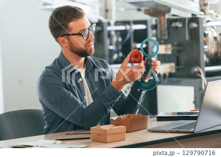 With an apple. Handsome man is working at the factory of creating eco boxes 129790716