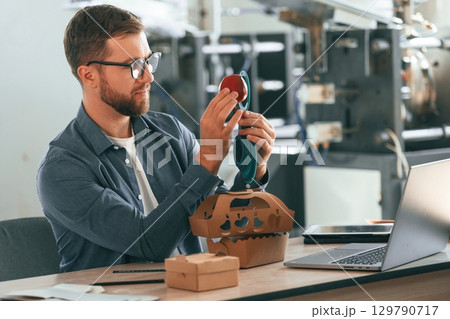 With an apple. Handsome man is working at the factory of creating eco boxes 129790717