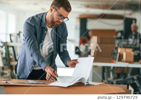 Document on the table. Handsome man is working at the factory of creating eco boxes Document on the table. Handsome man is working at the factory of creating eco boxes 129790729