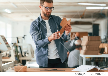 Document on the table. Handsome man is working at the factory of creating eco boxes Document on the table. Handsome man is working at the factory of creating eco boxes 129790732