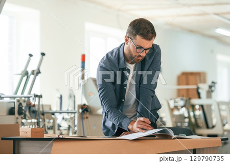Table, document on it. Handsome man is working at the factory of creating eco boxes Table, document on it. Handsome man is working at the factory of creating eco boxes 129790735