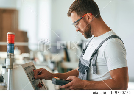 View from the side, using machine. Handsome man is working at the factory of creating eco boxes 129790770