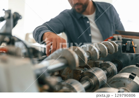 Metal made machine. Handsome man is working at the factory of creating eco boxes Metal made machine. Handsome man is working at the factory of creating eco boxes 129790806