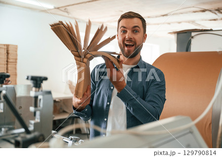 Bunch of cardboards in hands. Handsome man is working at the factory of creating eco boxes 129790814