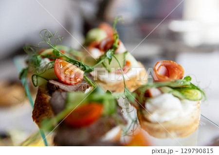 An assortment of elegant canapes with various meat and vegetable toppings on a glass tray. 129790815