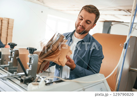 Bunch of cardboards in hands. Handsome man is working at the factory of creating eco boxes Bunch of cardboards in hands. Handsome man is working at the factory of creating eco boxes 129790820
