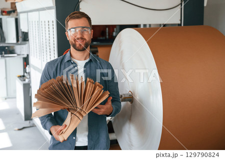 Many of the cardboards in hands. Handsome man is working at the factory of creating eco boxes 129790824