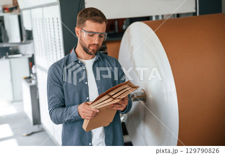 Many of the cardboards in hands. Handsome man is working at the factory of creating eco boxes Many of the cardboards in hands. Handsome man is working at the factory of creating eco boxes 129790826