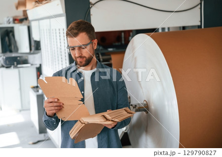 Many of the cardboards in hands. Handsome man is working at the factory of creating eco boxes 129790827
