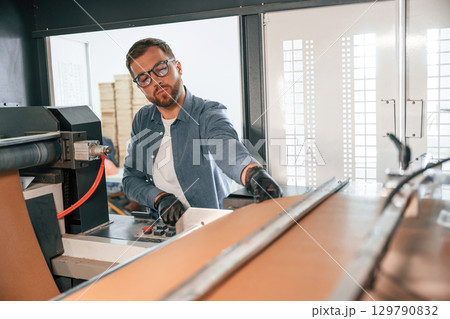 By the machine. Handsome man is working at the factory of creating eco boxes 129790832