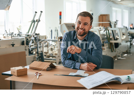 Sitting by the table. Handsome man is working at the factory of creating eco boxes Sitting by the table. Handsome man is working at the factory of creating eco boxes 129790857