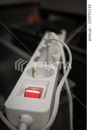 White electrical power strip with illuminated red switch and multiple outlets on a dark blurred 129791118