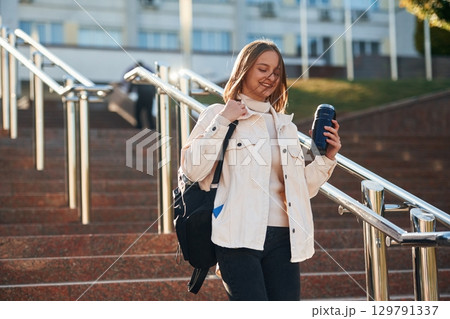 With water bottle. Young female student in casual clothes is outdoors 129791337