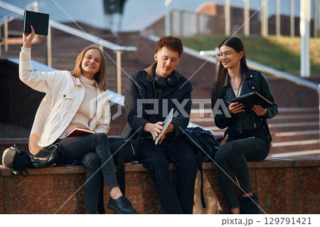With notepad. Three young students are outside the university outdoors With notepad. Three young students are outside the university outdoors 129791421