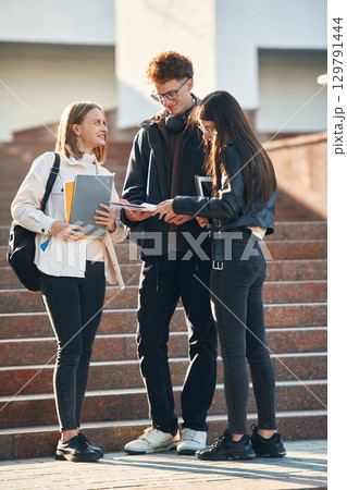 Holding notepads in hands. Three young students are outside the university outdoors 129791444