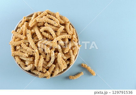 Traditional Indian snack murukku on blue background. Crispy treat made from rice flour and spices. Top view. Copy space Traditional Indian snack murukku on blue background. Crispy treat made from rice flour and spices. Top view. Copy space 129791536