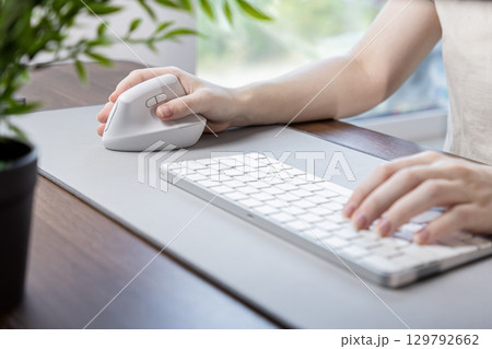 Person's hand operates a modern ergonomic vertical mouse and keyboard on a desk pad, emphasizing comfort and efficiency for prolonged remote work Person's hand operates a modern ergonomic vertical mouse and keyboard on a desk pad, emphasizing comfort and efficiency for prolonged remote work 129792662