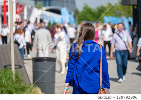 Woman walking in busy outdoor event with attendees and modern setting Woman walking in busy outdoor event with attendees and modern setting 129792906