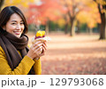 秋の味覚を楽しむ女性／紅葉の公園でスイーツを持つ笑顔の女性 129793068