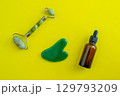 Bottle for cosmetics and jade massagers on a yellow background. Beauty saloon. Background with copy space. 129793209