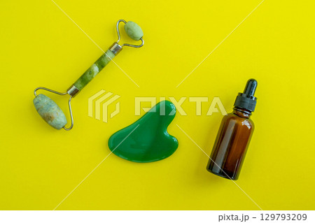 Bottle for cosmetics and jade massagers on a yellow background. Beauty saloon. Background with copy space. 129793209