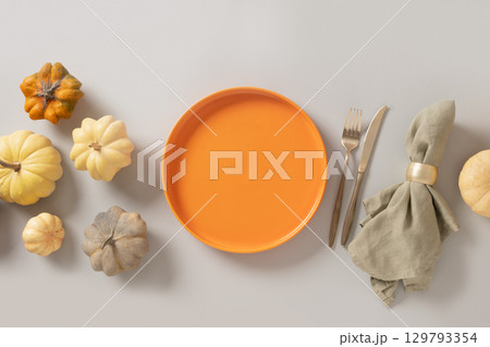 Autumn composition of colorful different small pumpkins, orange empty plate with golden cutlery on gray background. Harvest day, Concept catering or table setting. Top view. Thanksgiving Day. Banner. 129793354