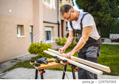 Mature male carpenter measuring wooden plank outdoors 129793569