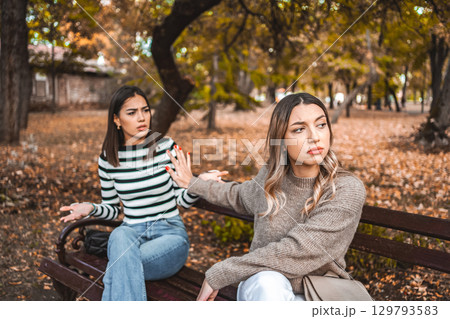 Two women are sitting on a bench and one does not want to listen to the other anymore 129793583