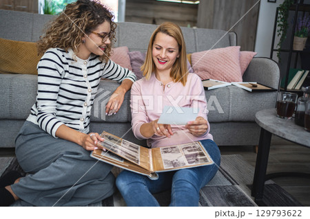 Two female friends looking at an old photo album at home Two female friends looking at an old photo album at home 129793622