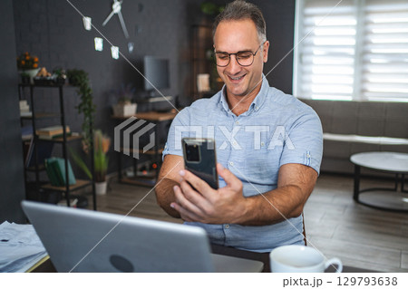 Middle aged Caucasian man using mobile phone and laptop at home 129793638