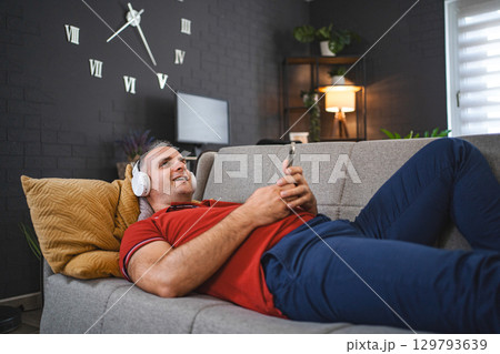 Middle age Caucasian man listening to music on the sofa Middle age Caucasian man listening to music on the sofa 129793639