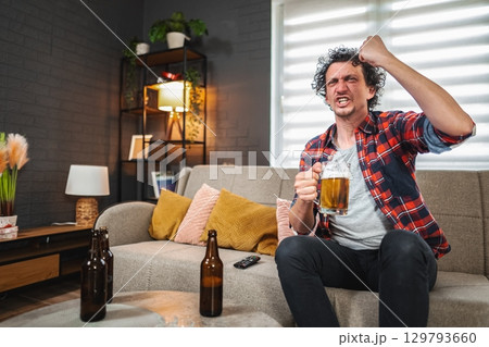 Excited sports fan celebrating with beer while watching tv at home Excited sports fan celebrating with beer while watching tv at home 129793660