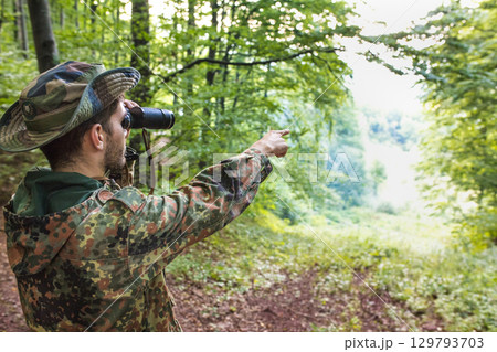 Soldier using binoculars and pointing in forest 129793703