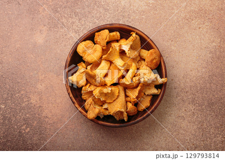 Fresh chanterelle mushrooms in a a rustic bowl on rustic brown background top view 129793814