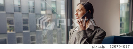 A Professional Woman Engaged in a Phone Conversation within a Modern Office Environment A Professional Woman Engaged in a Phone Conversation within a Modern Office Environment 129794017