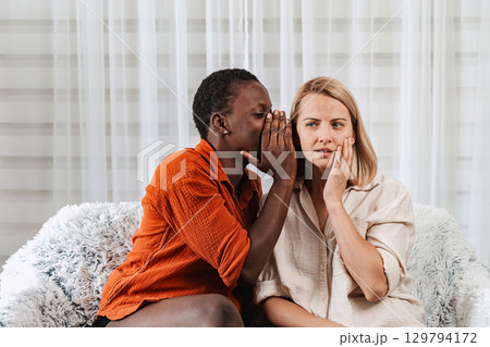 Young woman whispering a secret to her worried friend Young woman whispering a secret to her worried friend 129794172